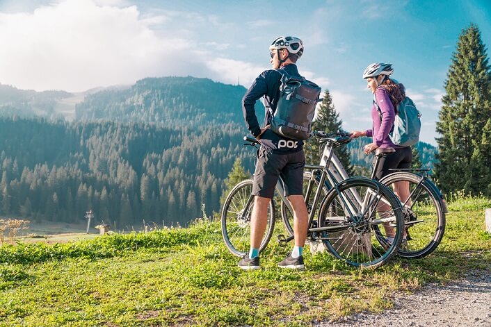 Two cyclists wearing helmets and backpacks enjoy a scenic mountain view.