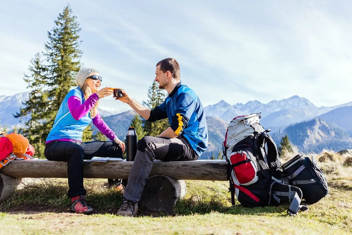A couple enjoying a break with drinks while hiking in the mountains.