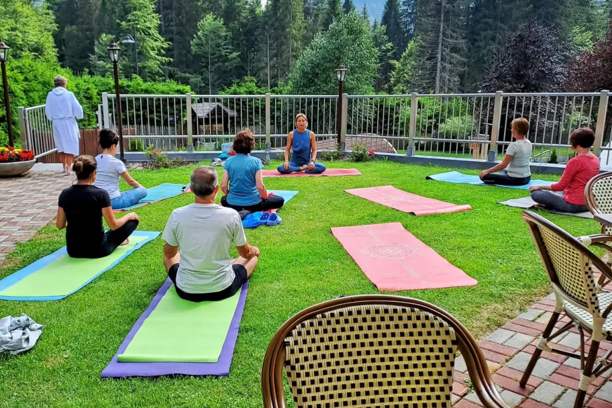 People practicing yoga outdoors on mats with a forest and mountain view.